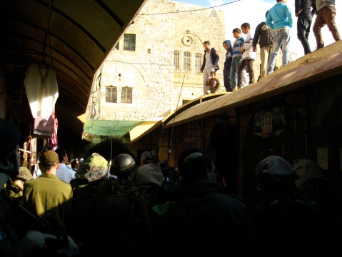Escorted settlers pass under Palestinians previously cleared from the streets. Photo credit: Brona McDonald